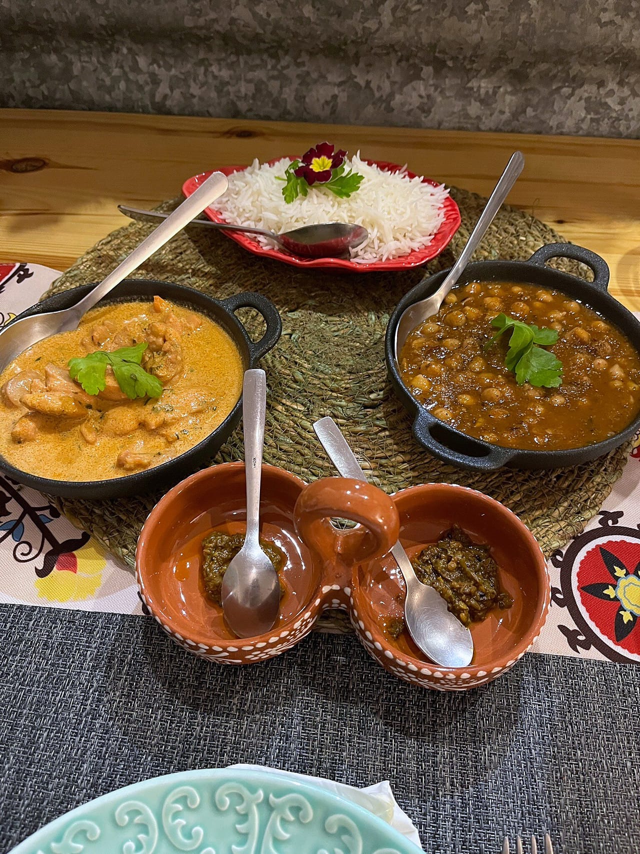 Dois caris em taças de metal, arroz basmati e pequenas taças de condimentos num tabuleiro