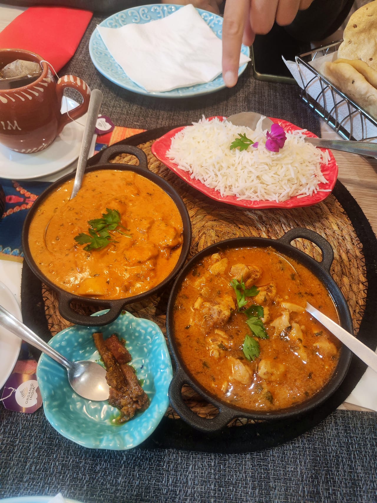 Dois caris em panelas de ferro, arroz basmati num prato vermelho e uma taça azul de pickle